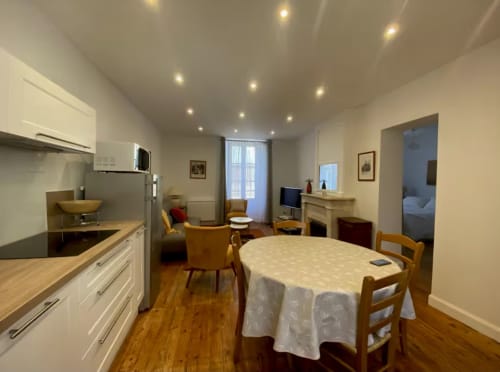 Spacious Le 58 Bayeux apartment with dining table, kitchen, living area with armchairs, and modern lighting.