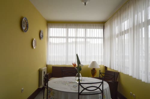 Sala de jantar amarelo brilhante com mesa redonda, vistas para o jardim e pratos decorativos na Casa Da Avó Ilda, Matosinhos