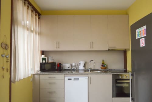Cozinha moderna da Casa Da Avó Ilda B&B com armários creme, lava-louças branco, forno, balcões de granito e paredes amarelas