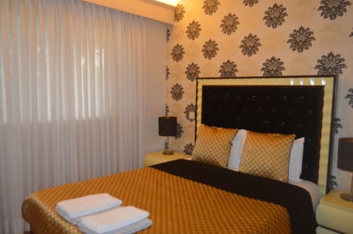 Quarto elegante da vila Casa Da Avó Ilda em Matosinhos com papel de parede damasceno dourado, cabeceira preta e roupas de cama douradas e aconchegantes