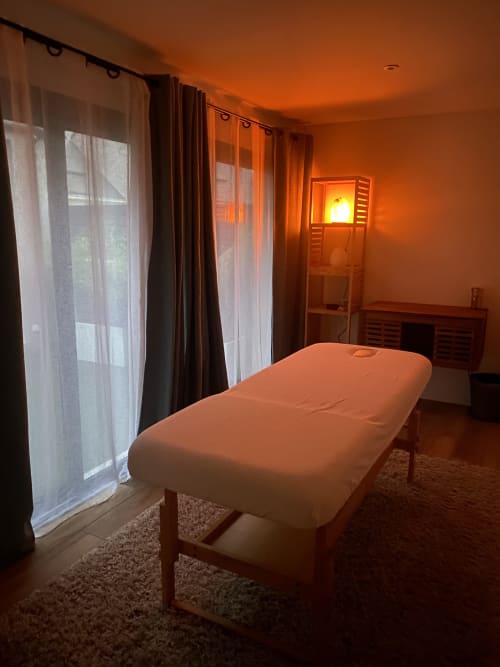 Spa-Massageraum im Gästehaus Lady Jule mit warmem orangefarbenem Licht, Massagetisch und großen Fenstern in Sainte-Luce-sur-Loire