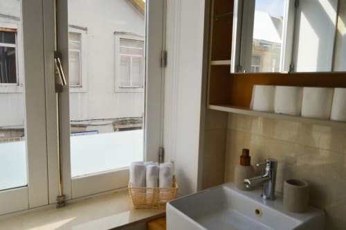 Banheiro moderno com pia branca, torneira cromada e cesto de toalhas enroladas na Casa Da Avó Ilda, Matosinhos