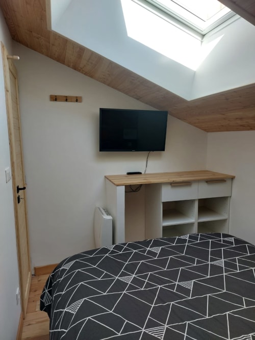 Chambre mansardée moderne à Méribel avec plafond bois en pente, lucarne, lit à motifs géométriques, TV murale et bureau en bois