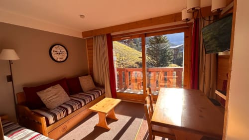 Séjour ensoleillé de l'appartement CMD Méribel Le Pralin avec vue montagne, canapé, mobilier bois et balcon aux Allues