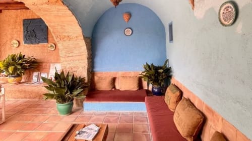 Patio de Can Gat Vell en Girona con puerta arqueada azul, azulejos de terracota, macetas y rincón rústico para descansar