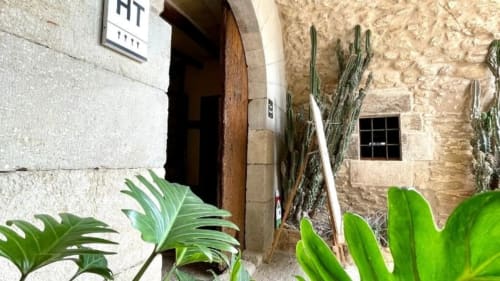 Entrada de Can Gat Vell en Girona con puerta de madera, muros de piedra y cactus en macetas