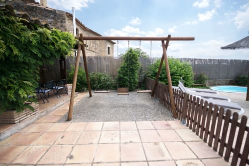Columpio rústico de madera en el patio de Can Gat Vell, casa rural en Girona con muros de piedra y vistas a la piscina