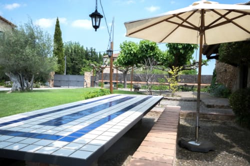 Piscina de Can Gat Vell con azulejos azules, sombrilla crema y vistas al campo del Empordà en Girona, Cataluña