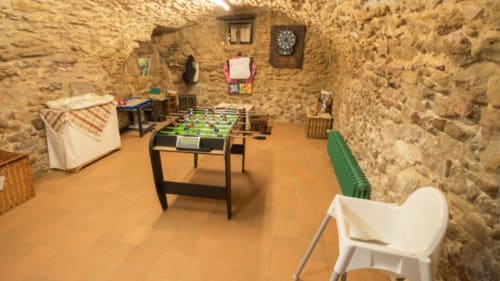 Sala de juegos en Can Gat Vell en Girona con futbolín, muros de piedra y suelo de barro rojo
