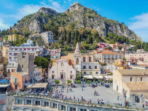 Piazza di Taormina con chiesa storica, edifici colorati e sfondo montano