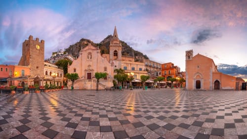 Piazza di Taormina al tramonto con chiese storiche e architettura mediterranea