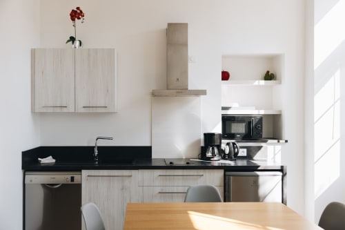 Cuisine moderne du gîte La Maison D'olivier avec plan de travail noir, placards en bois clair et coin repas avec table en bois
