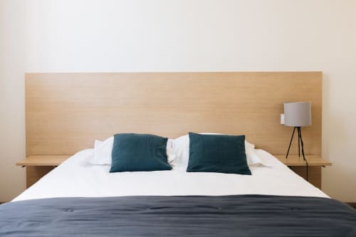 Chambre moderne avec tête de lit en bois, linge blanc, coussins bleu-vert et lampadaire trépied à La Maison D'olivier