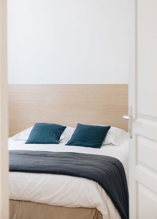 Chambre moderne à la maison d'hôtes La Maison d'Olivier à Mesnard-la-Barotière avec tête de lit en bois clair et coussins bleu-vert