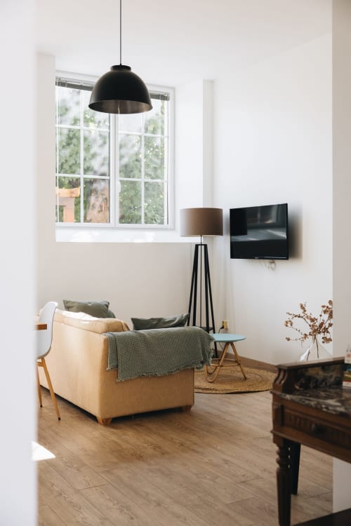 Salon moderne de la maison d'hôtes La Maison D'olivier avec fauteuil crème, lampe suspendue, TV et vue sur le jardin