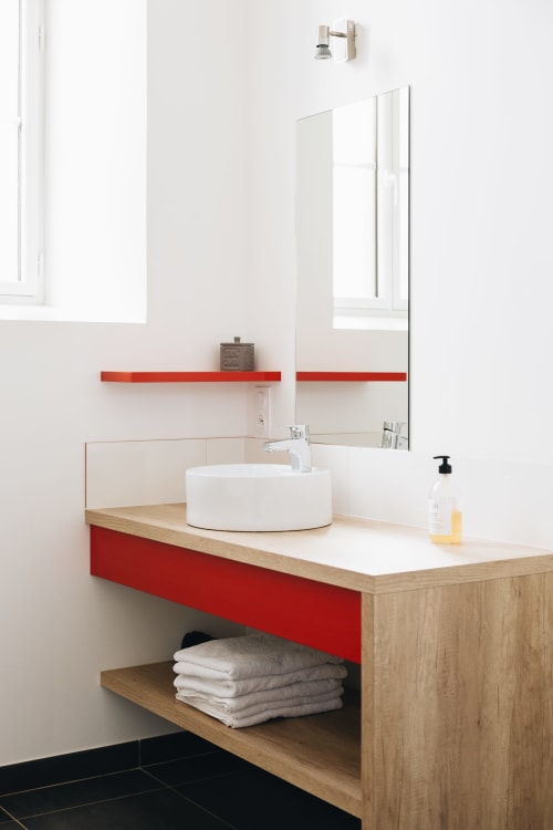 Salle de bains moderne de La Maison D'Olivier avec accents rouges, lavabo blanc, miroir et rangements en bois