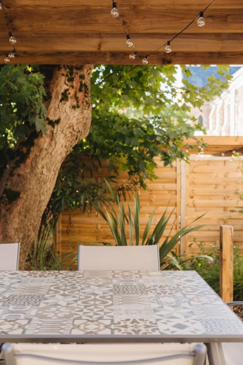 Espace de restauration en plein air à La Maison D'olivier avec pergola en bois, guirlandes lumineuses et ombre des arbres à Mesnard La Barotière