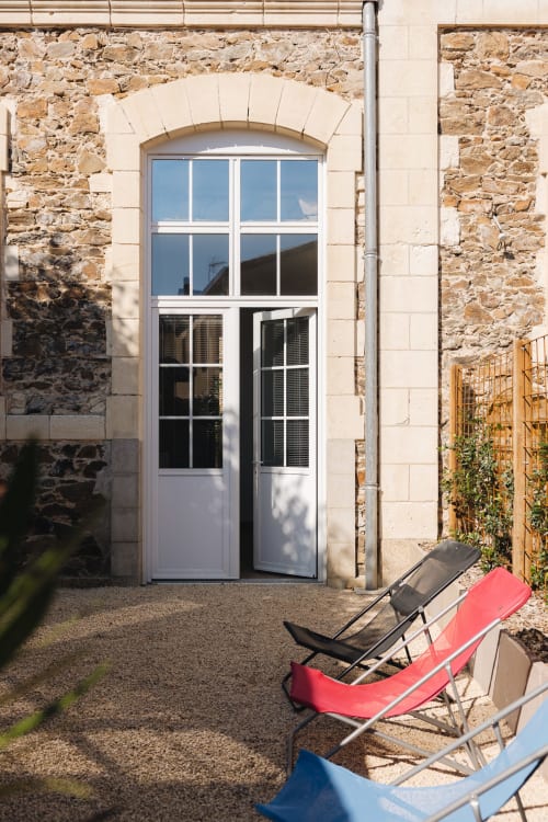 Cour en pierre de La Maison D'olivier avec porte blanche, fenêtre cintrée et transats colorés