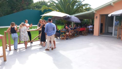 Guests socializing at La Conciergerie Biarritz terrace with umbrellas, lawn, and coral building in background