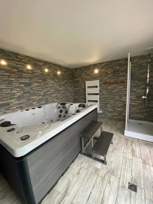 Salle de bain spa luxe au Domaine du Bez avec baignoire balnéo, douche pluie, porte-serviettes chauffant et murs en pierre.