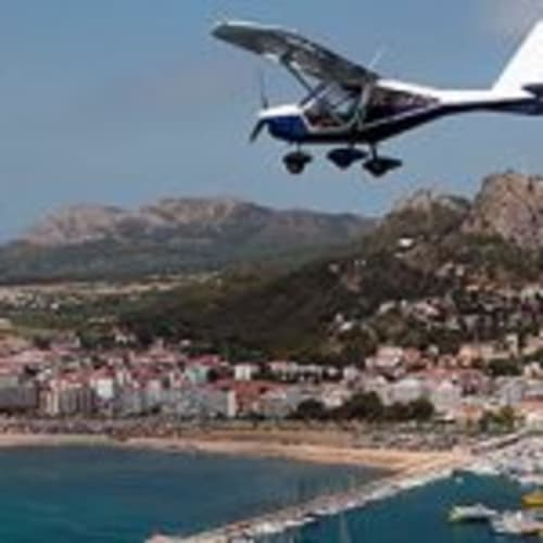 Small aircraft flying over coastal town with beach and mountains near Can Gat Vell, Girona