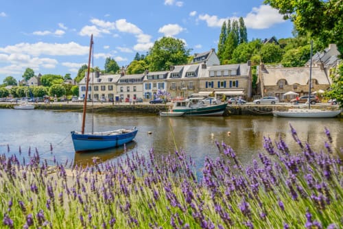 Charming harbor view with blue boat, purple flowers, and stone buildings at Les logis de Kergoulou in Concarneau