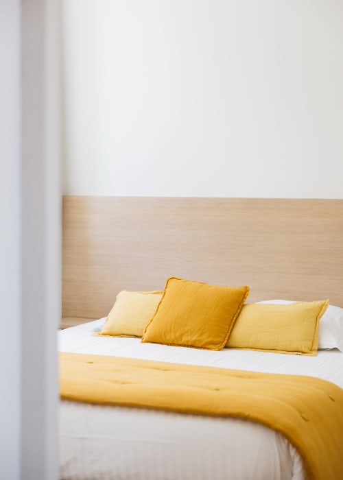 Chambre lumineuse à La Maison D'olivier avec oreillers et literie jaune doré sur une tête de lit en bois clair