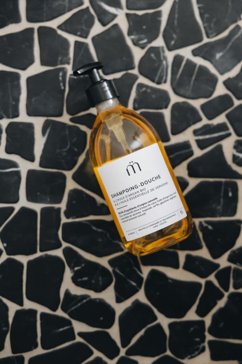 Flacon de shampooing-douche ambre avec distributeur à pompe noire sur surface géométrique à La Maison D'Olivier