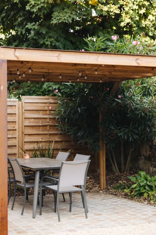 Terrasse extérieure de La Maison D'olivier avec table à manger, chaises, pergola en bois et jardin verdoyant à Mesnard La Barotière