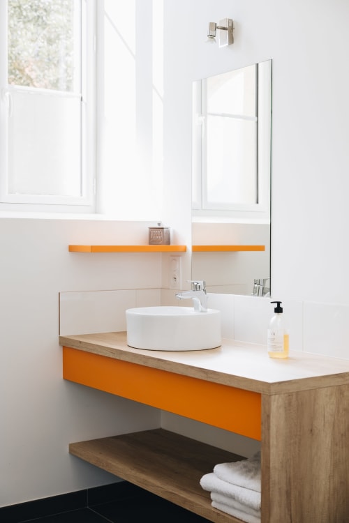 Lavabo moderne en céramique blanche avec accents orange, miroir et meuble-vasque en bois à La Maison D'olivier