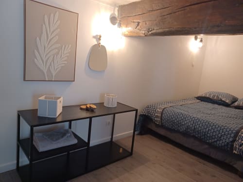 Chambre de l'appartement Accolade à Châteaudun avec lit, bureau noir, œuvres botaniques et poutres en bois rustique