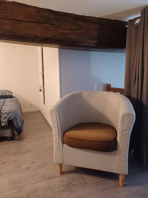 Chambre moderne à l'appartement Accolade à Châteaudun avec fauteuil crème et détails de poutre en bois