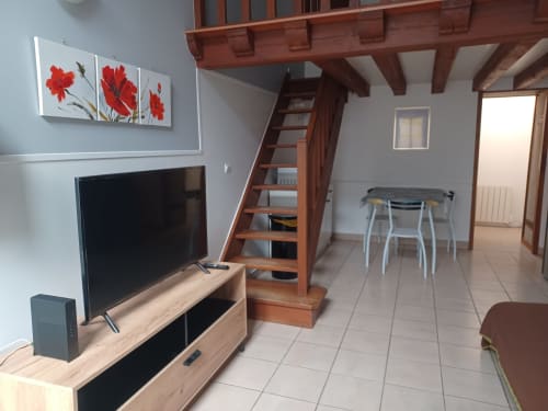Appartement loft moderne à Châteaudun avec escalier en bois, télévision, coin repas et tableau floral rouge