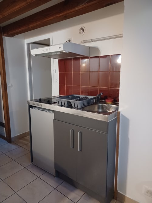 Kitchenette moderne de l'appartement Accolade à Châteaudun avec dosseret en carrelage rouge, plan de travail en inox et cuisinière à gaz