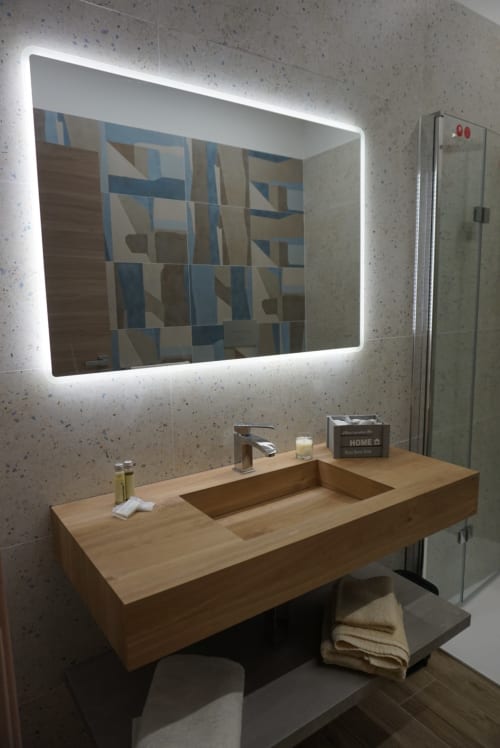Bagno moderno con specchio LED, lavabo in legno e rivestimento geometrico blu presso la boutique hotel La Dimora Di Ipno