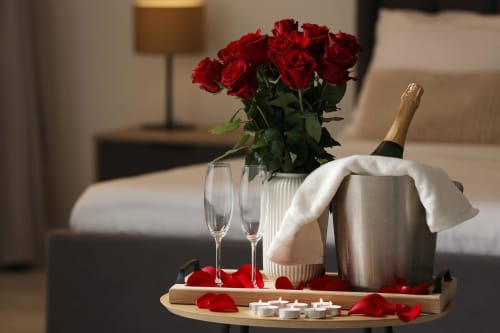 Suite romantique de l'hôtel Suite & Duplex avec roses rouges, flûtes à champagne, bouteille dans un seau à glaçons et pétales de roses