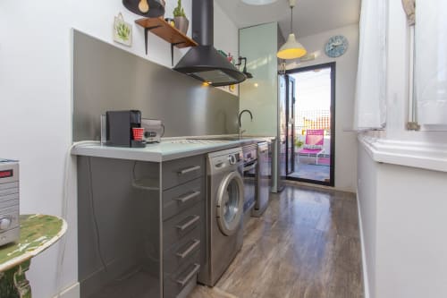 Cocina y zona de lavandería modernas en estudio Wehost Costaluz, Puerto Santa María con lavadora, estufa y balcón