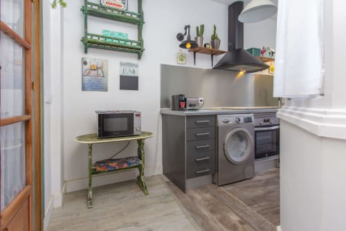Cocina moderna con electrodomésticos de acero inoxidable, estantes verdes, microondas y lavadora-secadora en apartamento de Puerto Santa María