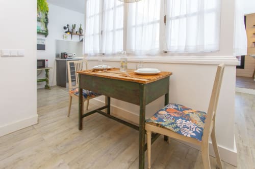 Luminosa cocina de apartamento con escritorio verde, sillas de madera con cojines estampados e iluminación natural desde las ventanas en Puerto