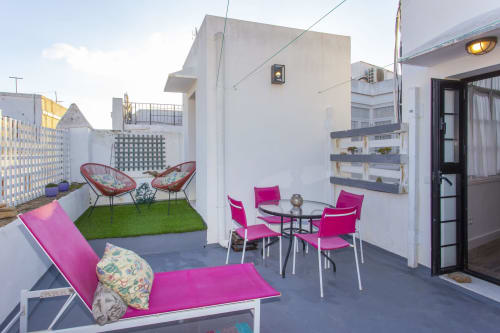 Luminosa terraza con asientos rosa, zona de césped artificial y vistas a la ciudad en apartamento de Puerto Santa María.