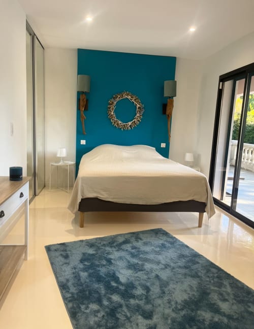 Modernes Schlafzimmer in der Villa des Ecureuils mit Teal-Akzentwand, weißer Bettwäsche und Türen zum Garten