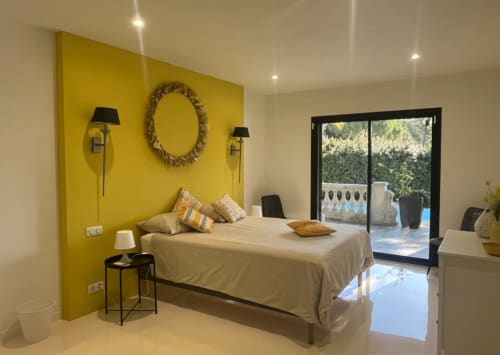 Modernes Schlafzimmer in der Villa des Écureuils mit gelber Akzentwand, cremefarbenem Bett und Terrassentüren mit Gartenblick in Boissieres