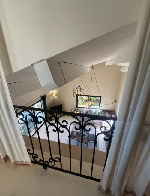 Zwischengeschoss mit verziertem schwarzem Geländer mit Blick auf den Lounge-Bereich der Villa La Conciergerie De Franck