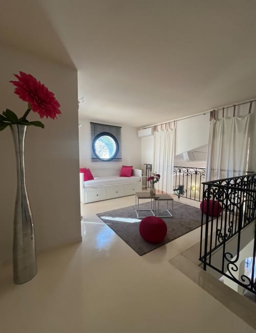Modernes Schlafzimmer mit rosa Dahlie, weißem Tagesbett, rundem Fenster und schwarzem Metallgeländer in La Conciergerie De Franck