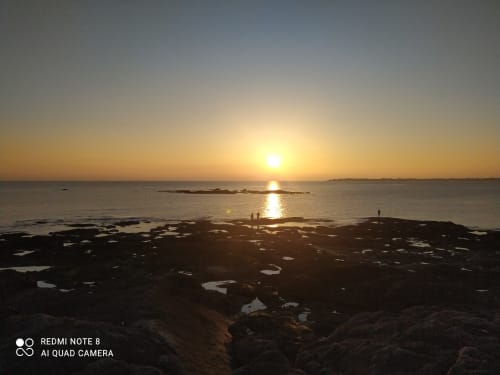 Coucher de soleil doré sur la plage rocheuse des Logis de Kergoulou à Concarneau, eaux calmes et îles lointaines