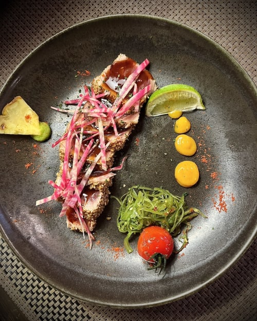 Assiette gastronomique du Le Maquis Plage : poisson poêlé, légumes marinés, agrumes et pousses sur ardoise noire.