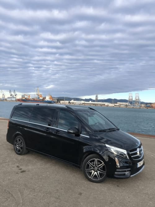 Furgoneta Mercedes negra estacionada en el puerto de Carboneras con buques de carga y montañas al fondo