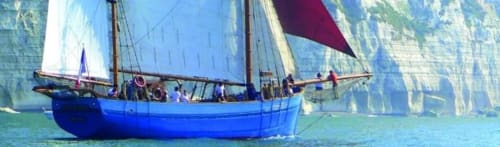 Blue traditional sailing boat on turquoise water near white cliffs in Étretat, France