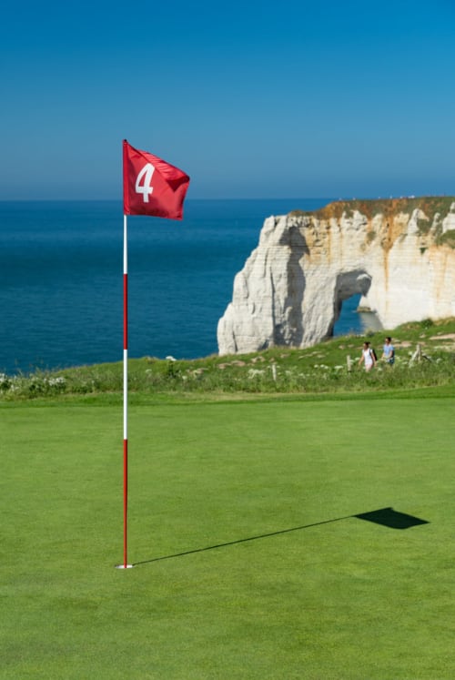 Golf hole with red flag marker overlooking dramatic white cliffs and ocean at Étretat, France