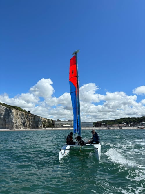 Sailboat with red and blue sail off Étretat coast with white cliffs, French Normandy coastal view